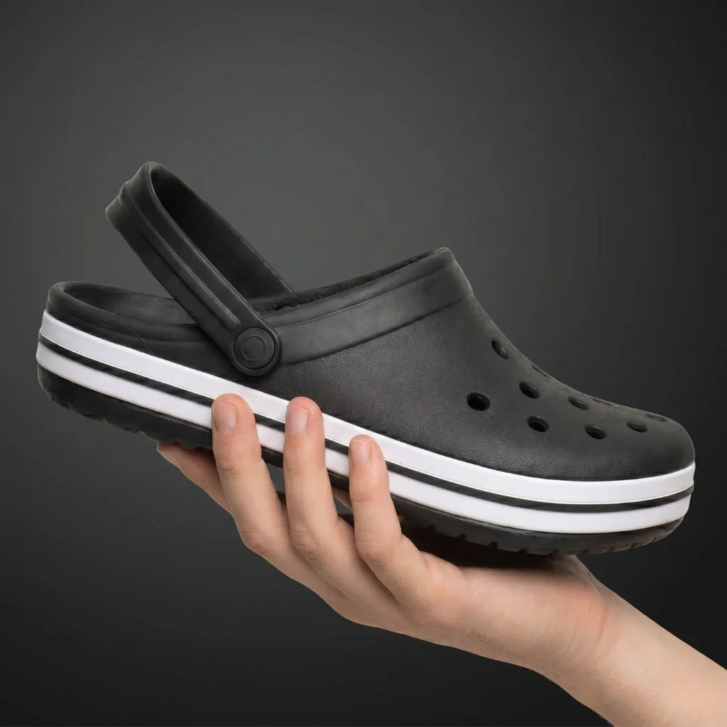 Chinelo preto com sola branca e furos, segurado na mão, ideal para conforto e estilo casual.